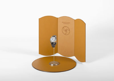 PLV et présentoir d'horlogerie luxe composé d'un socle en acier, d'un tapis de présentation, et d'un fond dépliable en cuir, créant une ambiance de studio photo qui place la montre en valeur et favorise l'image de marque.