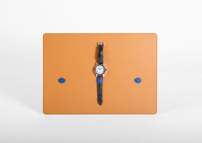 Plateau de présentation de montres en cuir comportant 3 bagues en cuir bleu. Une montre de luxe est tenue par son bracelet en cuir ouvert dans la bague centrale, qui la maintient en sécurité sur le plateau et favorise l'image de marque.
